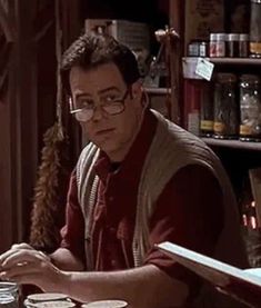 a man with glasses sitting at a table in front of a book shelf filled with books