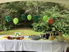 a table topped with lots of food and balloons in the air next to a forest