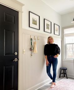 a woman standing next to a black door in a room with pictures on the wall