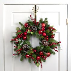 a christmas wreath hanging on a door with pine cones and red berries, holly berry balls and greenery