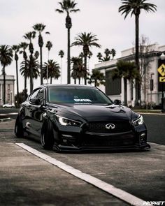 a black car parked on the side of a road next to palm trees and buildings