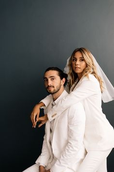 a bride and groom posing for a photo in front of a gray background with their arms around each other