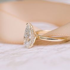 a yellow gold ring with a pear shaped diamond on it's side, sitting on a white surface