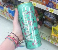 a person is holding up a can of soda in front of the store's shelves