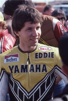 a man wearing a yellow and black motorcycle jacket in front of a crowd with other people