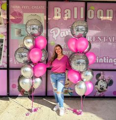 a woman standing in front of a balloon wall with pink, silver and black balloons