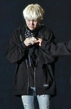 a woman with blonde hair is looking at her cell phone while standing in front of a black background