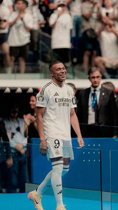 a man walking across a soccer field with his foot on the ground and people in the stands behind him