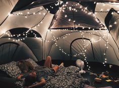 a person laying in a bed inside of a tent with lights strung from the ceiling