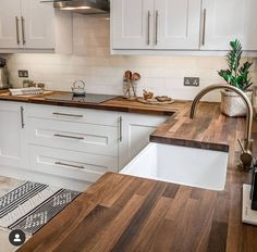 a kitchen with white cabinets and wood counter tops, an island sink and dishwasher