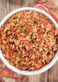 a white bowl filled with beans and vegetables on top of a wooden table next to a red cloth