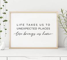 a white shelf with some plants and a framed poster on it that says life takes us to unexpected places live brings us home