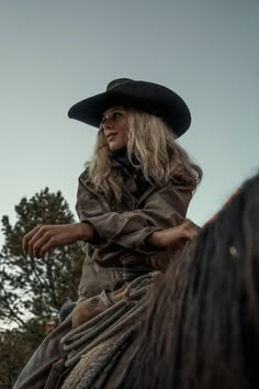 a woman riding on the back of a brown horse wearing a black cowboy hat and leather jacket