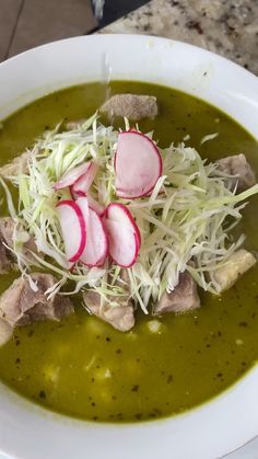 a white bowl filled with soup topped with meat and radishes