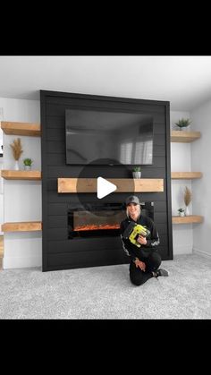 a man sitting on the floor in front of a fireplace with a television above it