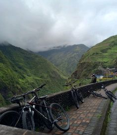 two bikes parked on the side of a road next to a wall with mountains in the background