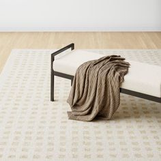 a white and black bench with a blanket on top of it in front of a wall