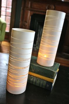 two white vases sitting next to each other on top of a table with text that reads, put plastic bands around a clear vase and spray paint it to turn a boring glass cylinder into something great