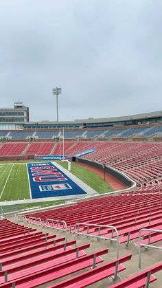 an empty stadium filled with red seats on a cloudy day in front of a football field