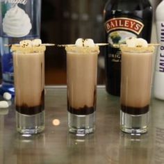 three glasses filled with chocolate and marshmallows on top of a table next to bottles