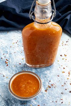 a glass jar filled with sauce sitting next to a small bowl full of something else