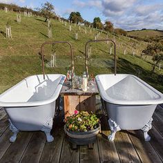 two bath tubs sitting on top of a wooden floor next to a table with flowers