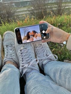 someone taking a selfie with their cell phone while sitting on the grass in front of some water