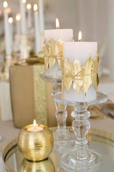 three candles are sitting on a glass tray with gold foiled leaves in the center