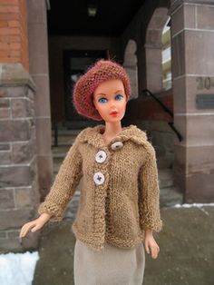 a doll is standing in front of a building with snow on the ground and brick walls