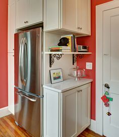 a stainless steel refrigerator in a kitchen with red walls and wooden floors, along with white cabinets