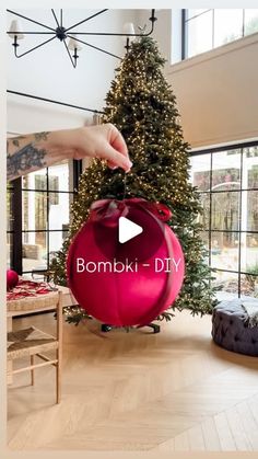 a person holding a red ball in front of a christmas tree