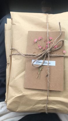 a package wrapped in brown paper tied with twine and pink flowers sitting on someone's lap