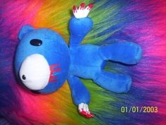 a blue stuffed animal laying on top of a rainbow colored furry material with red, white and green hair