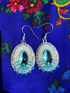 a pair of blue and white beaded earrings on top of a purple flowered cloth