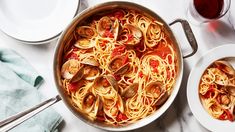 pasta with clams and sauce in a pan on a marble countertop next to two plates