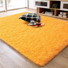 a bright yellow rug in the middle of a living room with pillows and coffee mugs on it