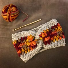 a crocheted headband next to a ball of yarn and a knitting needle