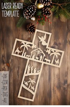 the laser - cut christmas scene is displayed on a wooden background with pine cones and evergreens