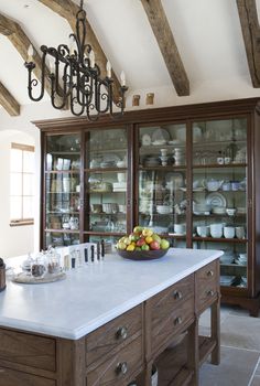 a large kitchen island with a bowl of fruit on it's top and glass front cabinets