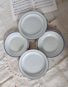 four white plates with blue trim sit on a doily next to an open book