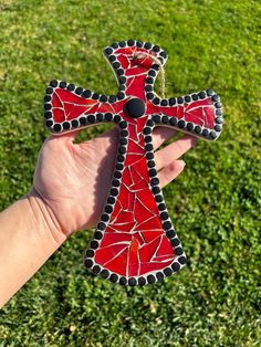 a hand holding up a red and black cross on top of green grass covered ground