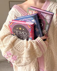 a woman holding three books in her hands while wearing a white sweater and pink pants