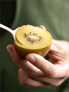 a person holding a kiwi fruit with a spoon in their hand to eat it