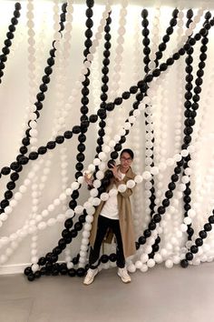 a woman standing in front of a wall with black and white balloons