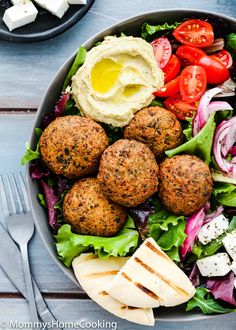 a salad with meatballs, lettuce, tomatoes and cheese on it next to some pita bread