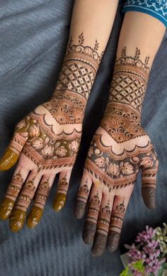 two hands with henna tattoos on them and flowers in the background, both showing their intricate designs