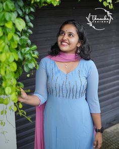 a woman wearing a blue dress standing in front of a green bush and smiling at the camera