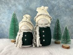 two knitted snowmen standing in front of small christmas trees on a snowy surface