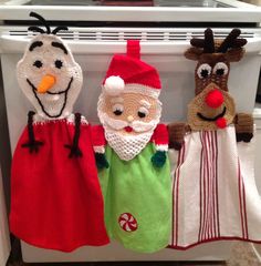 three knitted santa claus and reindeer dolls hanging on the oven door rack in front of an oven