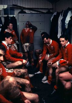 a group of men sitting around each other in a room with clothes hanging on the walls